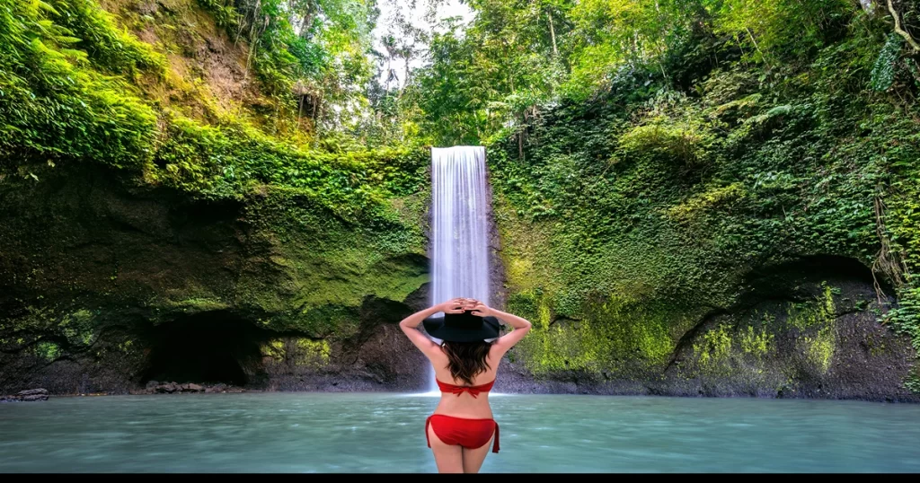 a woman standing Infront of water fall in swimming attire